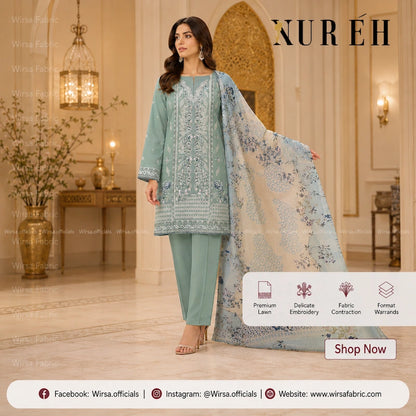 A woman models a traditional South Asian salwar kameez suit in a luxurious indoor setting. The outfit consists of a sage green kurta with intricate silver embroidery, matching green trousers, and a sheer light blue dupatta with blue floral patterns.